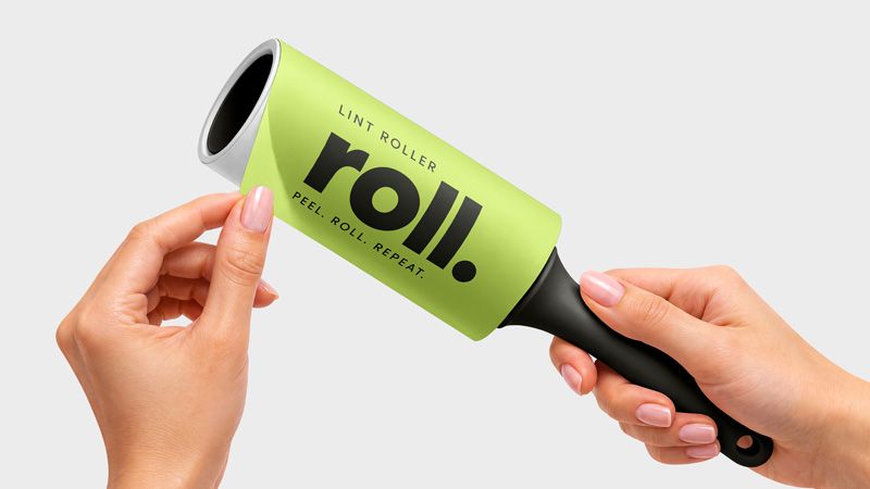 Lint roller mockup showing hands lifting a lime green protective wrapper with bold black lettering