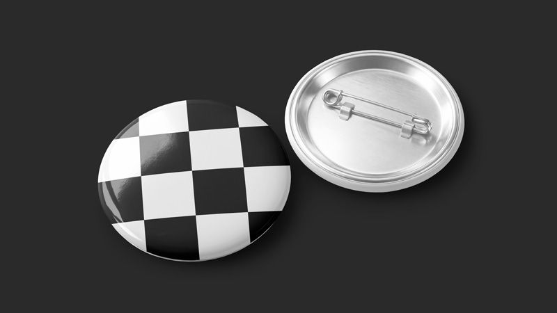 Round pin badge mockup with a black and white checkerboard face and a silver metal back on a dark background